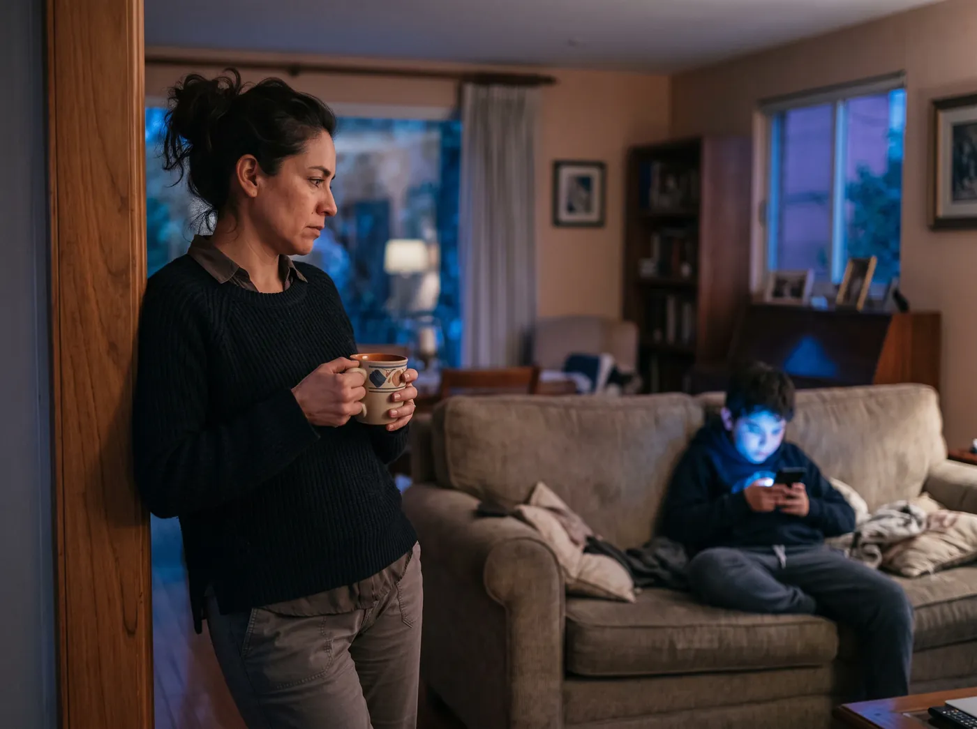Una madre observa pensativa a su hijo absorto en una pantalla.
