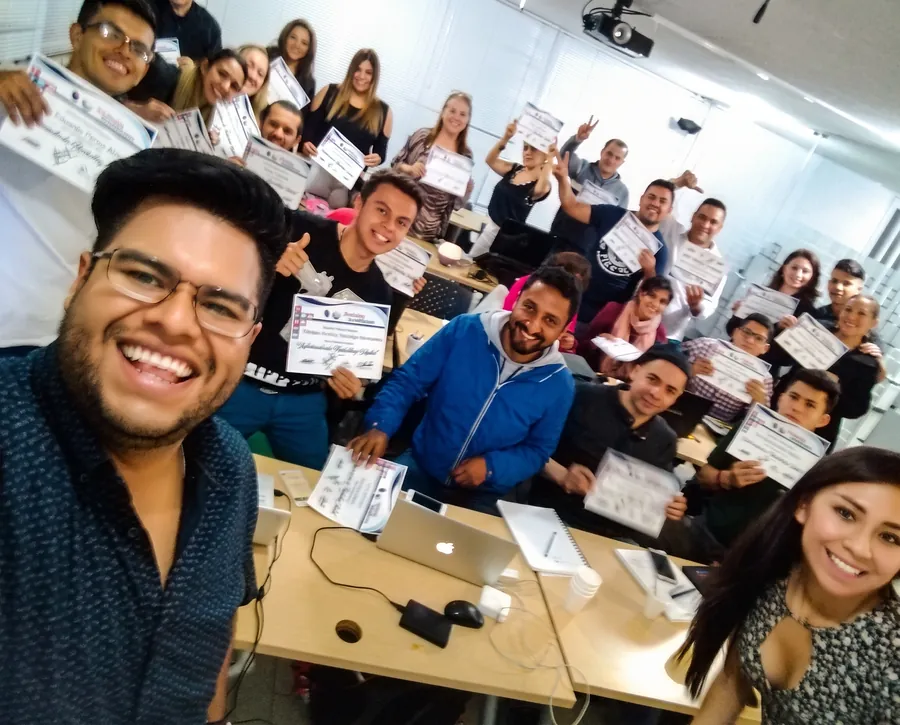 John Chávez con un aula llena de alumnos adultos mostrando sus certificados